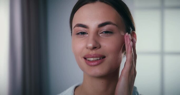 Close up of young female face. Portrait of beautiful woman gently touching soft delicate skin after face lifting rejuvenation procedure. Lady satisfied with new moisturising cream.