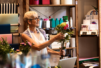 Senior woman working in flower shop making bouquet.