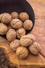 Large inshell walnuts fall from a dark cup on a wooden background.