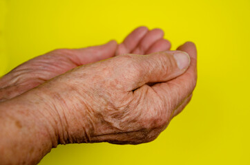 Fototapeta premium Old wrinkled hands. Kindness and mercy. Helping .Respect for elderly parents.Old hands on a yellow background. Granny is in need. Old age concept. Old hands ask for help. Wrinkled palms close up.