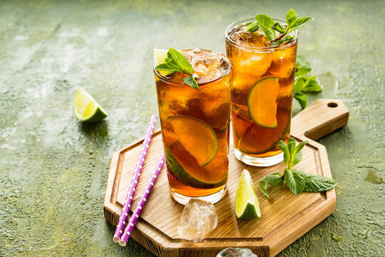 Refreshing drink, iced tea with lime wedges in glasses on a wooden board on a green concrete background. Summer drinks.