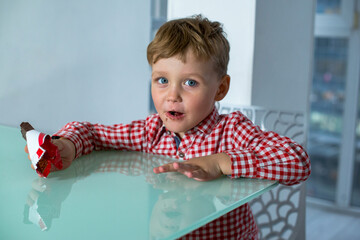 Boy eats a chocolate bar while sitting in kitchen.