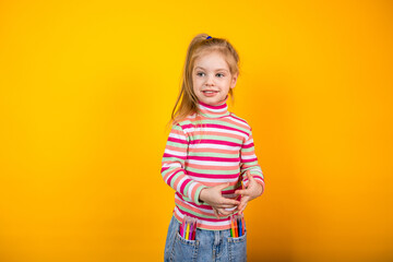 Young girl artist in a striped sweater standing on a yellow background with felt-tip pens in jeans pockets