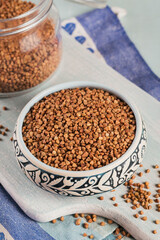 Organic uncooked scattered buckwheat grain in a bowl and glass jar on a light blue background
