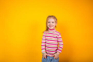 Funny little girl in a striped sweatshirt standing on a yellow background with markers in the pockets of her jeans