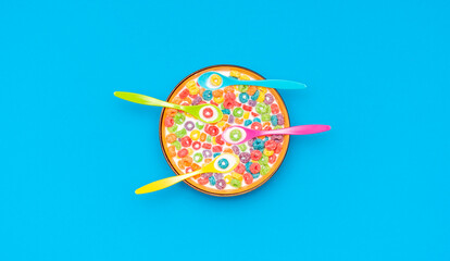 Fototapeta na wymiar Multicolored cereals and spoons in a bowl with milk, top view on a blue background.