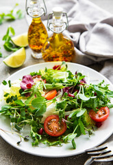 Fresh green mixed  salad bowl with tomatoes and microgreens  on  concrete background. Healthy food, top view.