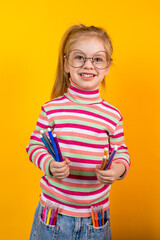 Young artist wearing glasses holding felt-tip pens standing against yellow background, vertical photo