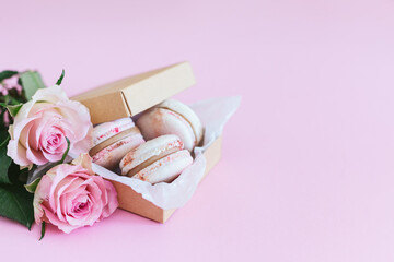 Obraz na płótnie Canvas Tasty french macaroons in a box with pink roses on a pink pastel background.