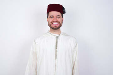 young handsome Caucasian man wearing Arab djellaba and Fez hat over white wall with a happy and cool smile on face. Lucky person.