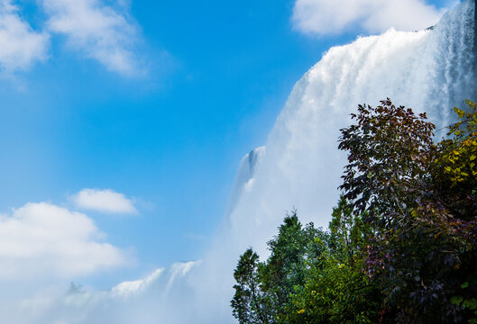 A low angle view of the Niagara falls with trees in the fore ground and blue sky in the background