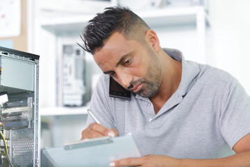 Obraz premium man holding mobile phone between ear while writing notes