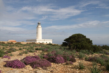 Faro de Cabo Salinas (Mallorca) con cielo azul ligeramente salpicado de nubes.