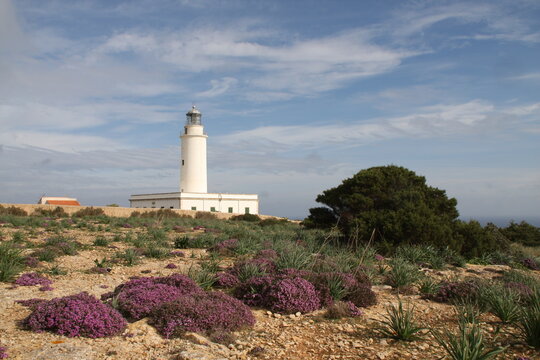 Faro de Cabo Salinas (Mallorca) con cielo azul ligeramente salpicado de nubes.