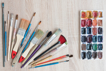 Obraz premium Top view of the artist's workplace. Diverse brush of different lengths and widths. Palettes with watercolors. Background, texture. Inspiration and idea