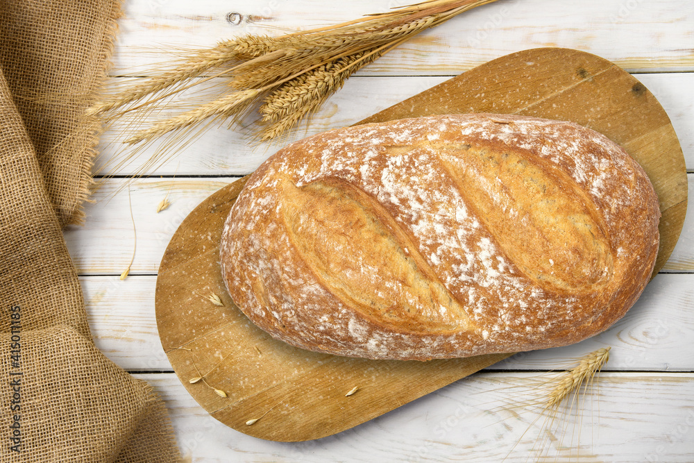 Wall mural rustic baking template - top view of a fresh baked bread on a wooden vintage cutting board with cere