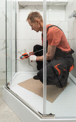 The worker is sealing the shower enclosure with silicone to prevent leakage.