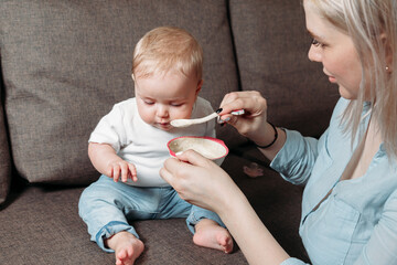 young mother feeds her son with a spoon of fruit puree
