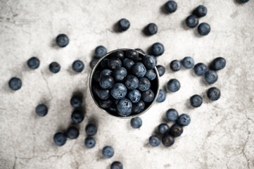 Fresh blueberries in a small metal bucket surrounded with some berries against concrete background. Top view. Rustic.