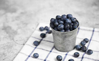Fresh blueberries in a small metal bucket surrounded with some berries on a checked napkin. Top view. Rustic.