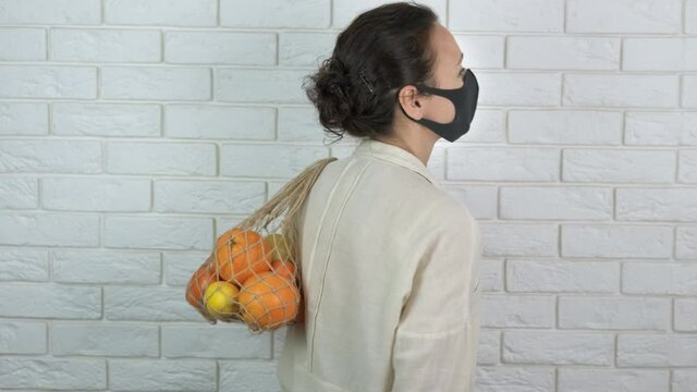 Farmer vitamines in quarantine. A woman with a protective mask with a string bag of fruits on her back.