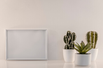 Modèle de cadre photo blanc avec espace vide pour logos, inscription publicitaire. Cadre en mode paysage sur un espace de travail avec des plantes vertes. 
