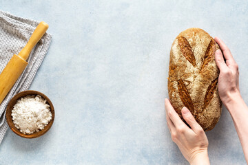 Woman's hands holding homemade fresh bread. Bowl of flour on stone background. Top view, copy space.