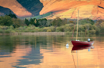 Moored yacht with autumn fells reflected in placid lake surface