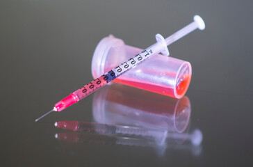 A syringe and a vial containing red fluid is shown on a glass table