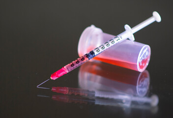 A syringe with a vial of red fluid is shown on a glass table