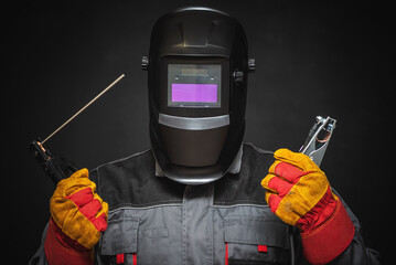 A welder in a helmet with a welding terminals in hand on a black background.