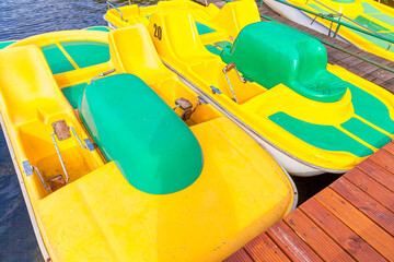 Pedal boats or paddle boats catamarans station. Yellow water bicycles locked at lake marina dock pier on sunny summer day. Summer leisure activity outdoors.