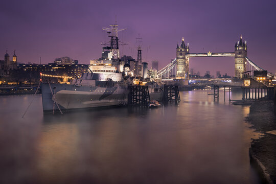 HMS Belfast with Tower Bridge in background, shot early morning with Thames Mist and city lights, London