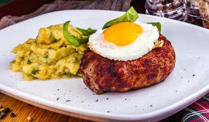 Grilled steak with fried egg and mashed potatoes on white plate