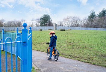 School kid learns to ride a bike in the Park, Portrait of a lonely little boy on bicycle alone on the grass fields, Sad Child in helmet riding a cycling standing near playground.
