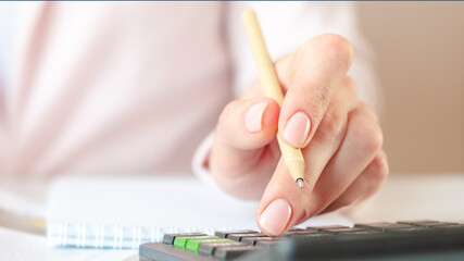 close up of woman hand with calculator counting and taking notes to notebook