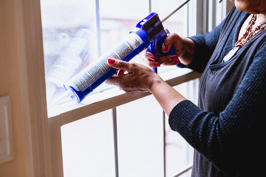 Black Senior woman weather sealing, caulking windows for winter
