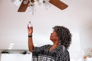 Black senior woman installing energy efficient LED light bults, DIY