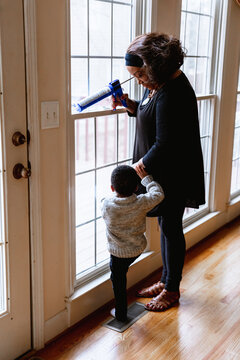 Black grandmother woman weather sealing, caulking windows for winter with toddler grandson