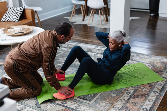Senior woman doing sit-up exercises with husband, active lifestyle fitness
