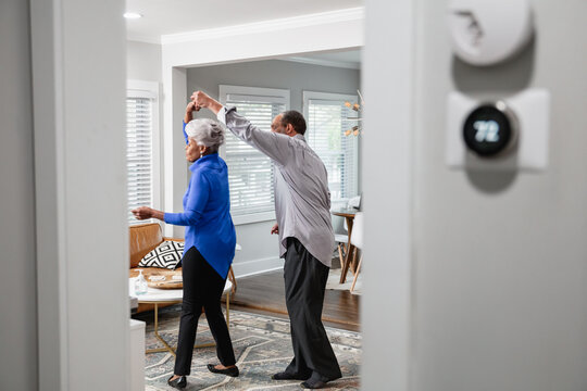 Black senior couple enjoys retirement at home dancing to music, smart thermostat