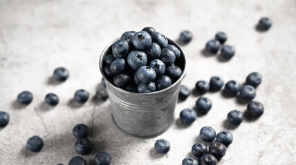 Fresh blueberries in a small metal bucket surrounded with some berries against concrete background. Top view. Rustic.
