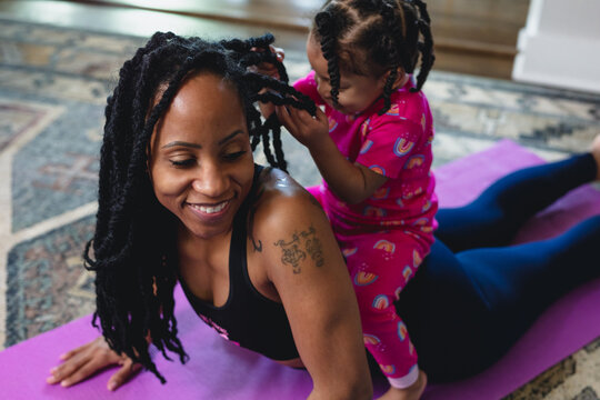 Smiling mid-30s mother and happy toddler at home on yoga mat, exercising and playing