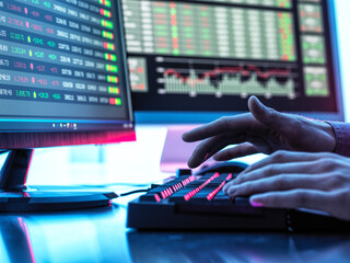 Hands of trader typing on keyboard in front of computer monitor displaying stock market data