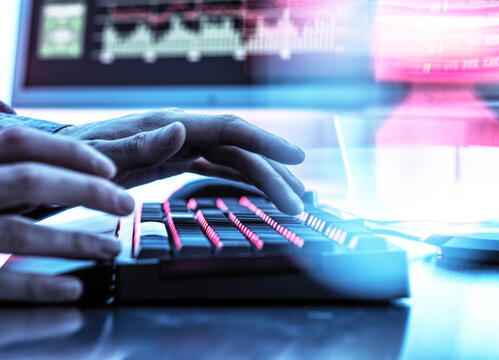 Hands of trader typing on keyboard in front of computer monitor displaying stock market data