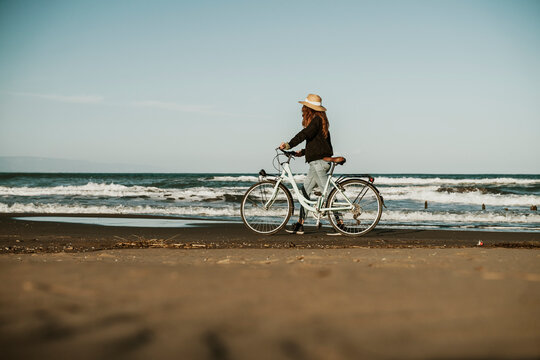 Young woman walking with bicycle by water waves at Fangar Beach, Ebro delta, Spain