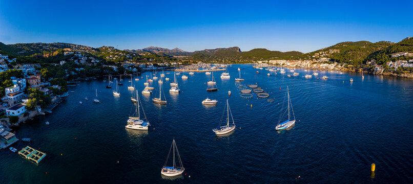 Spain, Mallorca, Andratx, Helicopter view of boats sailing near shore of coastal town at summer dusk