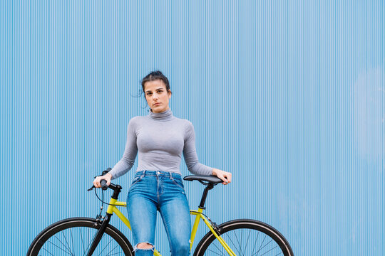 Confident mid adult woman sitting on fixie bike against blue wall