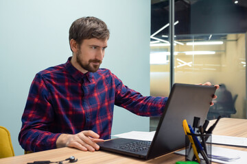Portrait of a young man working on a laptop in a co-working office. Consultation, online training, business