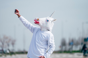 Man wearing unicorn mask taking a photo with smartphone